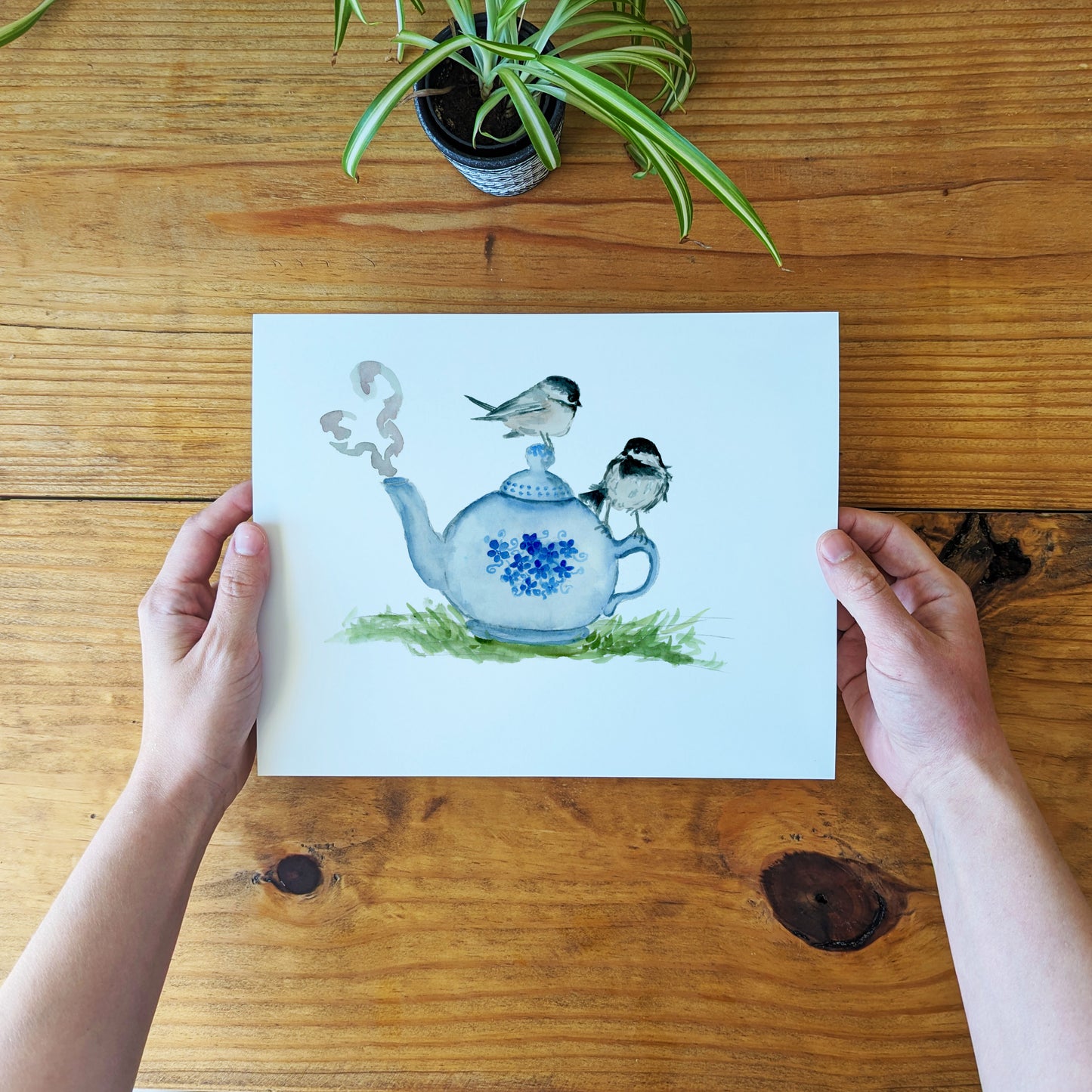 a person holding a card with a picture of a teapot and birds on it