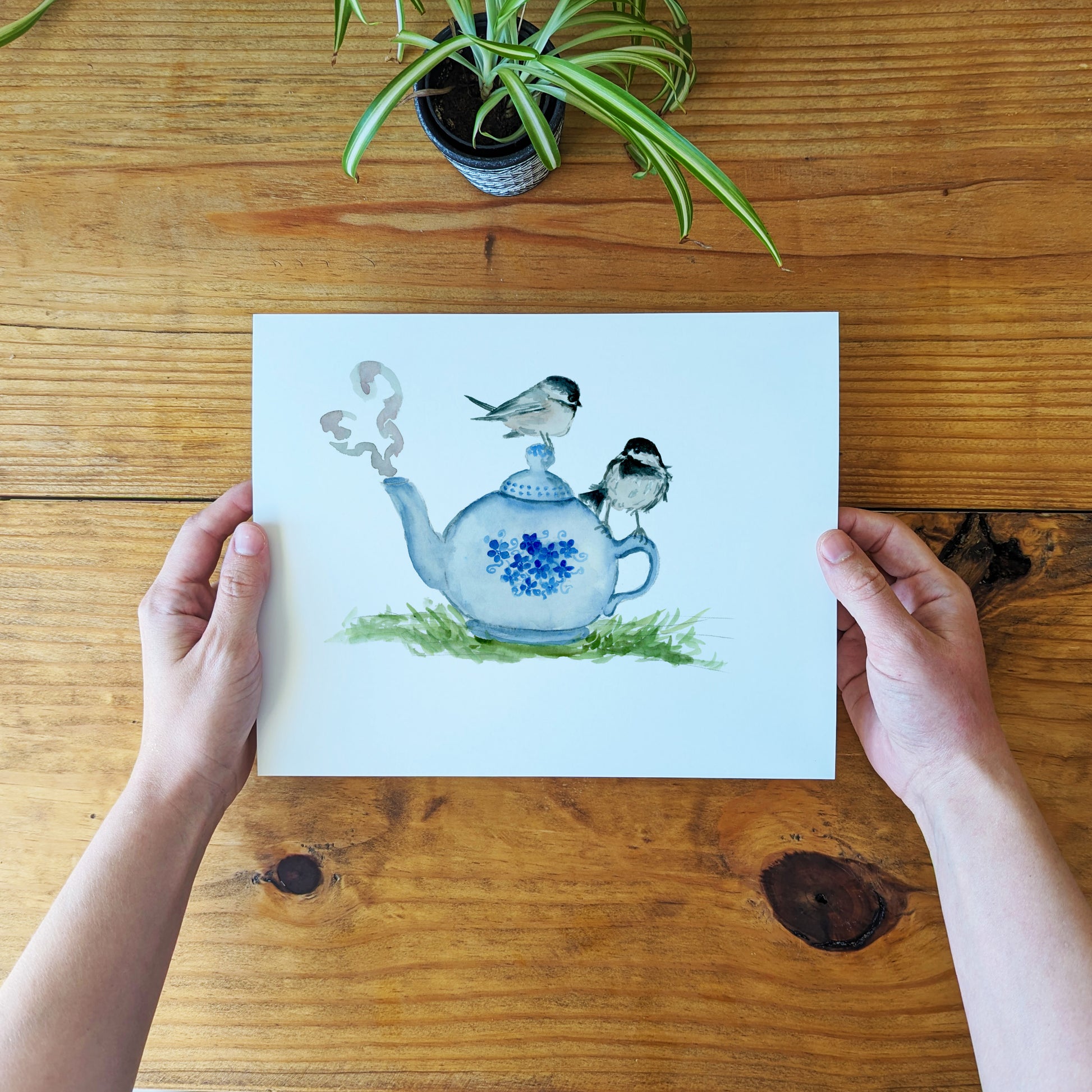 a person holding a card with a picture of a teapot and birds on it