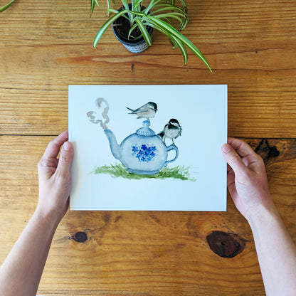 a person holding a card with a picture of a teapot and birds on it