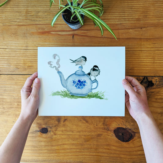 a person holding a card with a picture of a teapot and birds on it