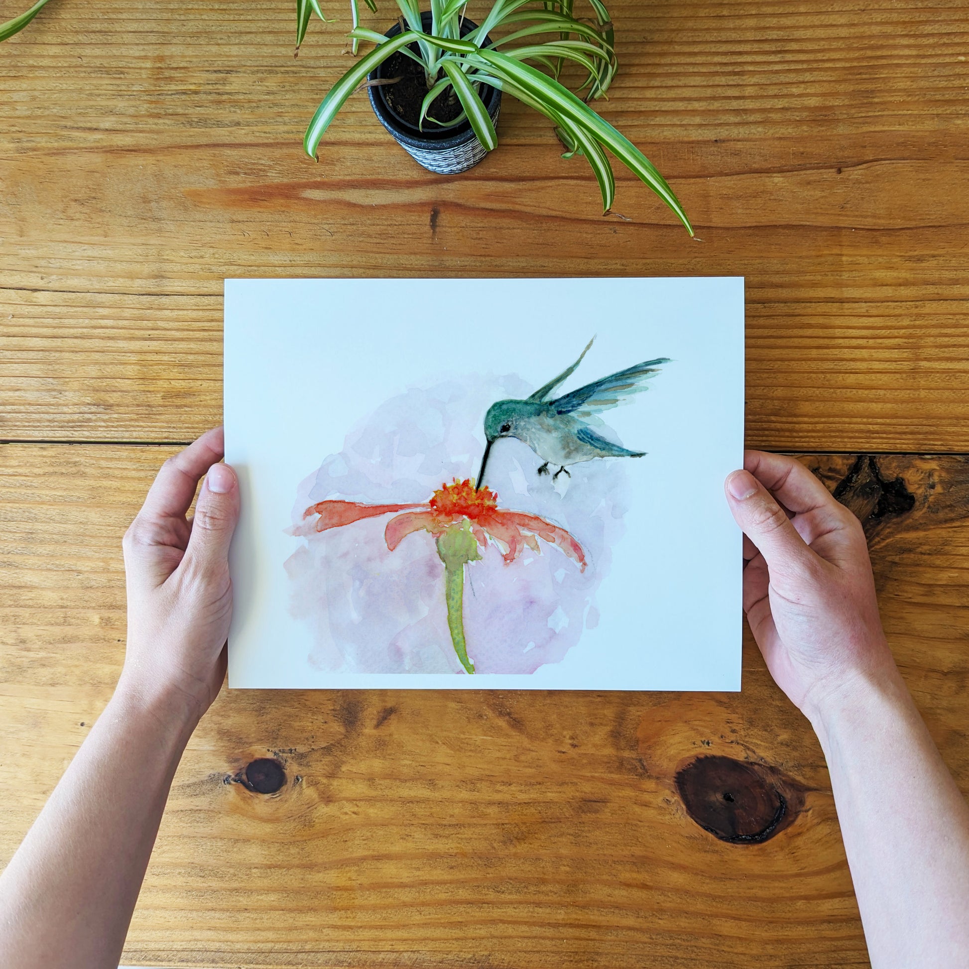 a person holding a piece of paper with a painting of a hummingbird on it
